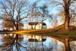 Hovedbygningen på Hellviktangen på Nesodden sett gjennom trær, med speilbilde i en dam i forgrunnen.