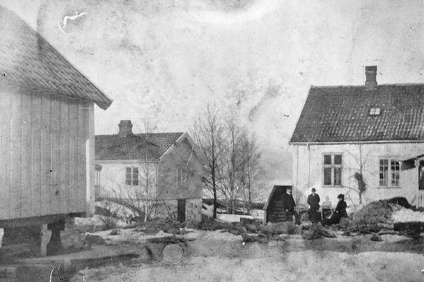 Svart-hvitt bilde av bygninger og mennesker ved Hellviktangen på Nesodden rundt 1900, med trehus, uthus og gårdsplass.